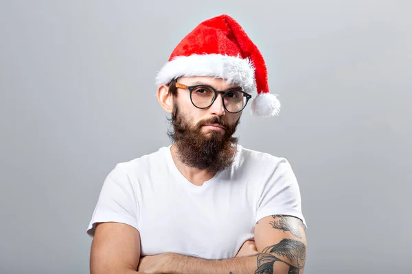 Urlaub und Menschen - Porträt eines gutaussehenden brutalen Mannes mit Weihnachtsmütze. vor grauem Hintergrund. — Stockfoto