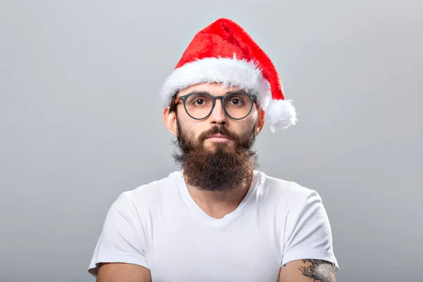 छुट्टियों और लोगों की अवधारणा क्रिसमस टोपी में एक सुंदर क्रूर आदमी का चित्र। ग्रे पृष्ठभूमि पर . — स्टॉक फ़ोटो, इमेज