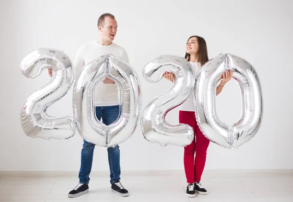 New year, celebration and holidays concept - love couple having fun with sign 2020 made of silver balloons for new year on white background