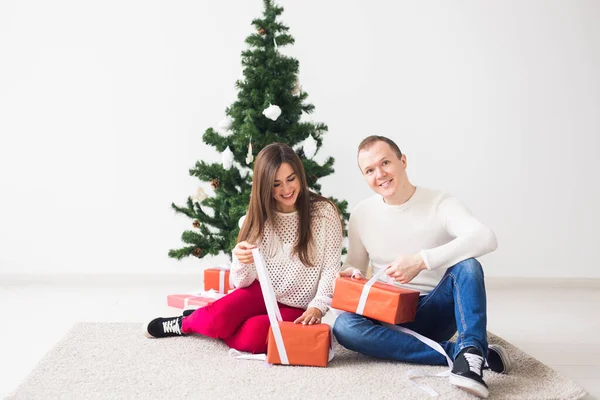 Navidad, vacaciones y concepto de celebración - Hombre joven y guapo joven sentado en la alfombra y están sosteniendo una caja de regalo — Foto de Stock