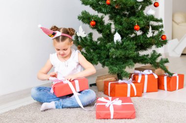 Çocuk Noel hediyelerini açıyor. Noel ağacının altında hediye kutularıyla çocuk.