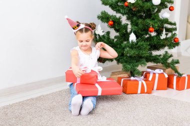 Çocuk Noel hediyelerini açıyor. Noel ağacının altında hediye kutularıyla çocuk.