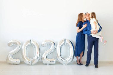 Genç, mutlu aile babası ve kızı beyaz arka planda 2020 numaralı balonların yanında duruyorlar. Yeni yıl, Noel, tatil