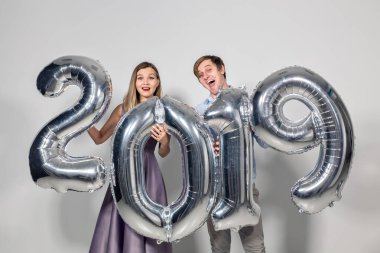 Yeni yıl, kutlama ve tatil konsepti. Yeni yıl için gümüş balonlardan yapılmış 2019 tabelasıyla eğlenen aşk çifti.