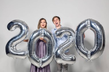Yeni yıl, kutlama ve tatil kavramı. Yeni yıl için gümüş balonlardan yapılmış 2020 tabelasıyla eğlenen aşk çifti.