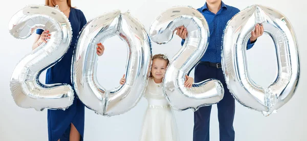 Joven familia feliz madre y padre e hija sosteniendo globos en forma de números 2020 sobre fondo blanco. Año nuevo, Navidad, vacaciones — Foto de Stock