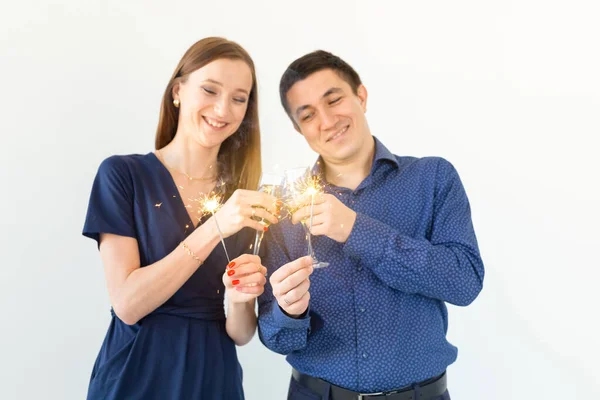 Uomo e donna che festeggiano il Natale o il Capodanno con luci del Bengala e bicchieri di champagne su sfondo bianco . — Foto Stock