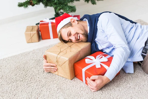 圣诞和假日的概念- -戴着圣诞礼帽的快乐男人在客厅里打开礼物 — 图库照片