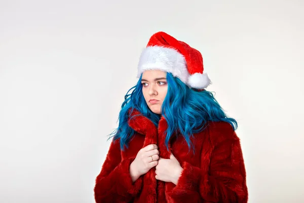 Beyaz arka planda poz veren kırmızı kürklü ve Noel Baba şapkalı komik beyaz kadın. Mavi saçlı neşeli bir kadın model. Fotoğraf çekiminde eğleniyor.. — Stok fotoğraf