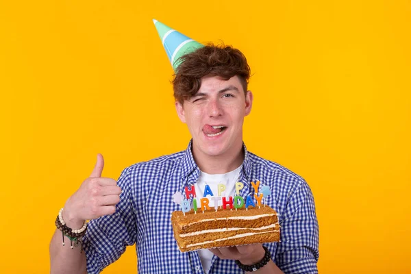 Jovem positivo segurando um bolo de aniversário feliz posando em um fundo amarelo . — Fotografia de Stock