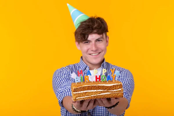 Joven positivo sosteniendo un pastel de cumpleaños feliz posando sobre un fondo amarillo . —  Fotos de Stock