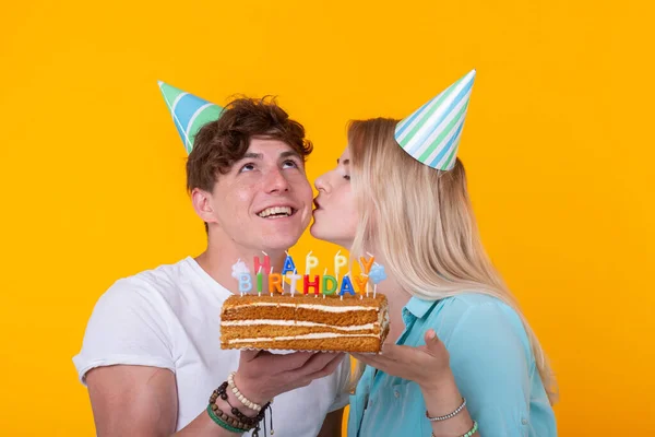 Engraçado nerd homem e mulher estão usando feriados bonés e óculos segurando bolo de aniversário com velas sobre fundo amarelo — Fotografia de Stock