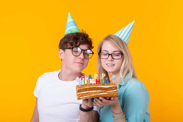 Забавный ботаник мужчина и женщина носят праздничные колпачки и очки с праздничным тортом со свечами на желтом фоне — стоковое фото