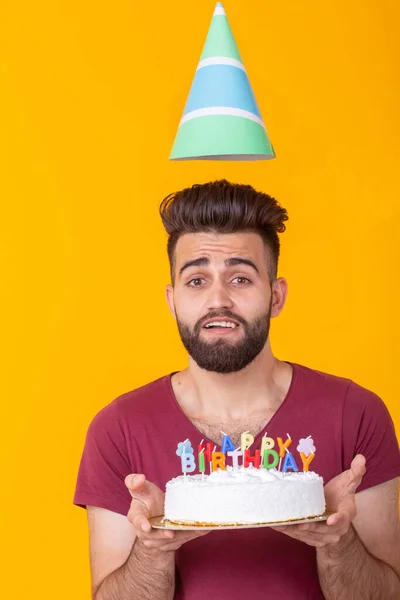 Young male hipster with a beard holding a cake with the inscription happy birthday congratulations on the anniversary and the holiday. Concept of promotions and discounts.