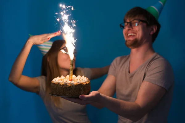 벵골 불꽃 촛불 케이크를 들고 인사 종이 모자에 젊은 쾌활한 학생 매력적인 소녀와 좋은 사람. 생일과 기념일에 축 하의 개념 — 스톡 사진