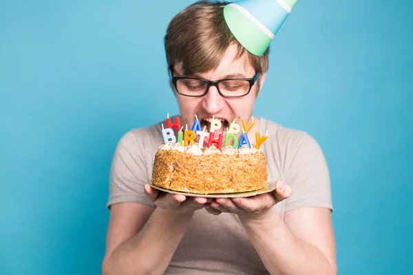 Divertente giovane pazzo in un cappello di carta augurale vuole mordere un pezzo di torta di congratulazioni. Concetto di scherzare e auguri di compleanno. Copia spazio — Foto Stock