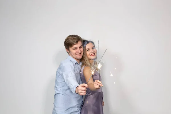 Conceito de férias, família e celebrações - abraço de casal jovem com bengalas cruzadas luz ou brilhos no fundo branco — Fotografia de Stock