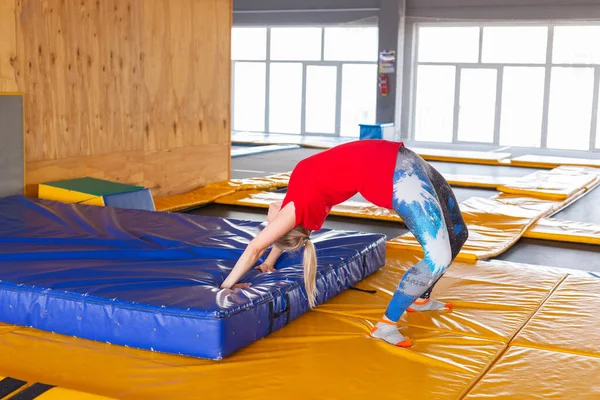 Young woman sportsman on a trampoline in fitness park and doing exercise indoors — Stock Photo, Image