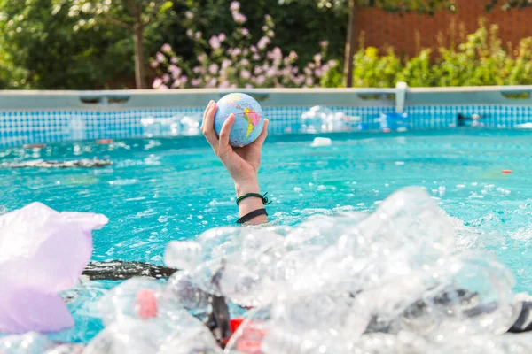 Ufa, Rusland-25 juli 2019: probleem van de Prullenbak, kunststof recycling, vervuiling en milieu concept-plastic vuil vervuiling in watermilieu, Earth Globe drijft in de Prullenbak — Stockfoto