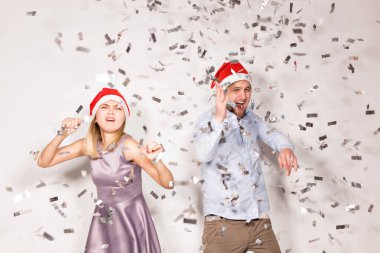 Yeni yıl, Noel ve parti konsepti - Neşeli gençler beyaz arka planda konfeti yağmuruna tutuldu.
