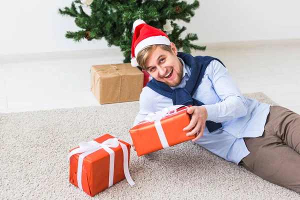 Noel et concept de vacances - Joyeux homme au chapeau de Père Noël ouvrant un cadeau à la maison dans le salon — Photo
