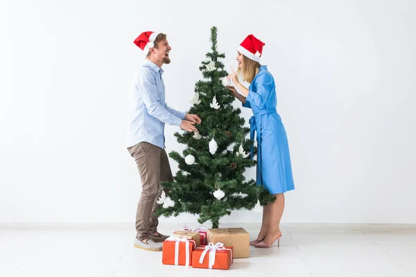 Holidays and festive concept - Young family couple in santa hats decorating the christmas tree — ストック写真