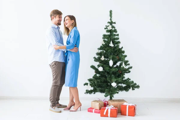 Tatiller ve festival konsepti - Genç mutlu çift beyaz arka planda bir Noel ağacının yanında — Stok fotoğraf