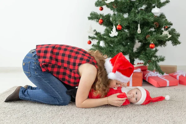 假期和圣诞节的概念-年轻的母亲在圣诞树前抱着孩子桑塔爪 — 图库照片