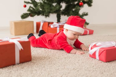 Noel Baba kostümü giyen tatlı bir bebek Noel ağacının üzerinde sürünüyor. Tatil sezonu.