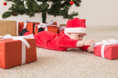 Noel Baba kostümü giyen tatlı bir bebek Noel ağacının üzerinde sürünüyor. Tatil sezonu.