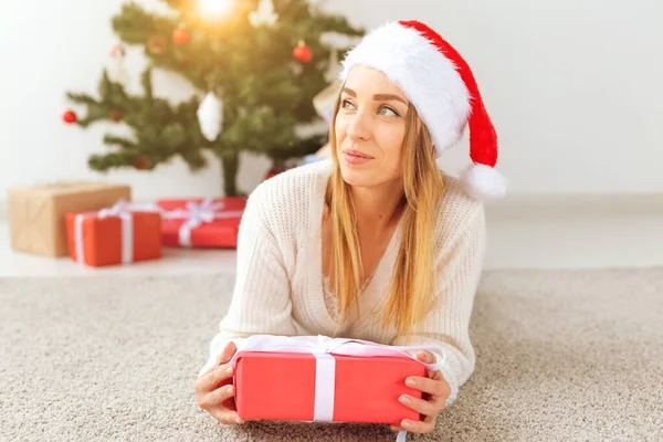 예쁜 금발 여성 이 따뜻 한 뜨개 질 스웨터를 입고 거실에 있는 크리스마스 트리 근처 카펫에 누워 있습니다. 나무 밑에 많은 선물 이 있어. — 스톡 사진