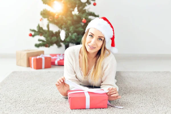 Mulher loira bonita vestindo uma camisola de malha quente, deitada em um tapete perto da árvore de Natal decorada em uma sala de estar. Muitos presentes debaixo da árvore . — Fotografia de Stock