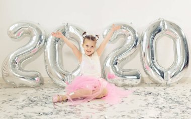 Yeni yıl, tatiller ve kutlama konsepti - 2020 numaralı balonlarla birlikte oturan küçük kız