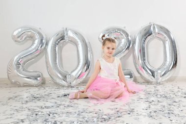 Yeni yıl, tatiller ve kutlama konsepti - 2020 numaralı balonlarla birlikte oturan küçük kız