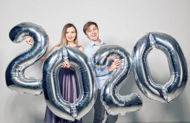 Yeni yıl, kutlama ve tatil kavramı. Yeni yıl için gümüş balonlardan yapılmış 2020 tabelasıyla eğlenen aşk çifti.