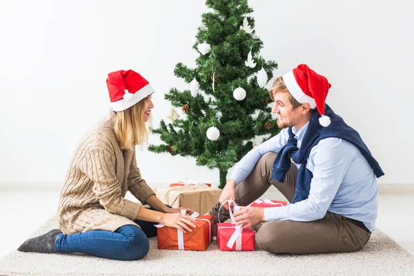 Ünnepek koncepció - Édes pár nyitó karácsonyi ajándékok, ül a nappaliban — Stock Fotó