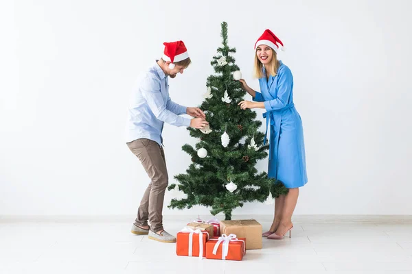 Tatiller ve festival konsepti Noel Baba şapkalı genç bir çift Noel ağacını süslüyor. — Stok fotoğraf