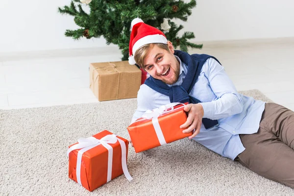 Koncepcja świąt Bożego Narodzenia i świąt - szczęśliwy człowiek w kapeluszu Mikołaja otwierający prezent w domu w salonie — Zdjęcie stockowe