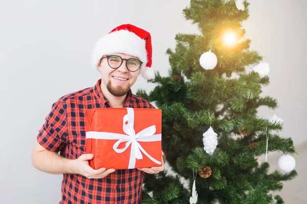 Koncepcja świąt Bożego Narodzenia i świąt - Śmieszny człowiek w kapeluszu Mikołaja trzymający prezent w domu w salonie — Zdjęcie stockowe