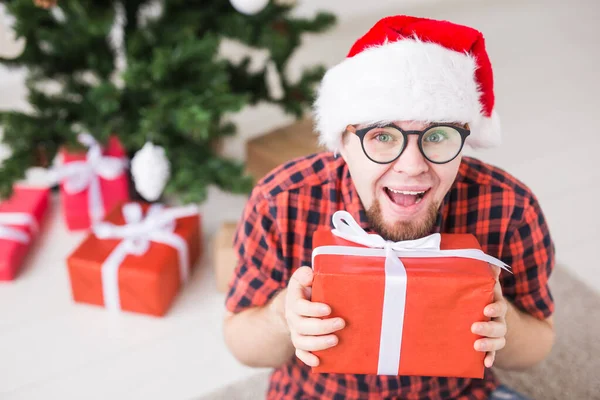 Kerstmis en feestdagen concept - Grappige man in santa hoed met een geschenk thuis in de woonkamer — Stockfoto