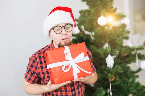 クリスマスと休日のコンセプト-サンタの帽子の面白い男はリビングルームで家で贈り物を持っています — ストック写真