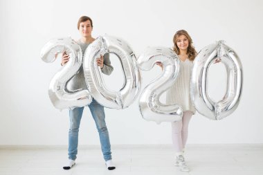 Bayramlar, şenlik ve parti konsepti mutlu çift öpücükleri ve beyaz arka planda gümüş 2020 balon tutmaları. Yeni yıl kutlaması