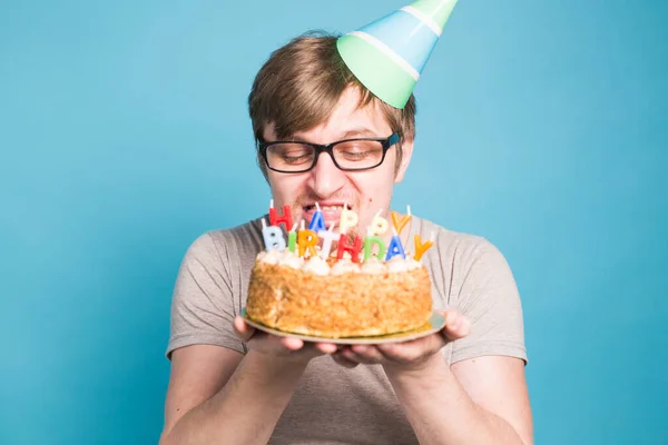 Divertido joven loco en un sombrero de papel de saludo quiere morder un pedazo de pastel de felicitación. Concepto de bromas y felicitaciones de cumpleaños. Copiar espacio —  Fotos de Stock