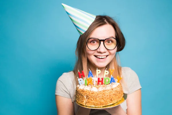 파란색 배경에 서 그녀의 손에 생일 케이크를 들고 축하 종이 모자에 매력적인 메리 미친 어린 소녀 학생. 광고 공간. — 스톡 사진