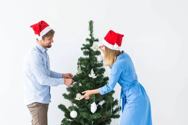 Ünnepek és ünnepi koncepció - Fiatal család pár télapó kalapban díszíti a karácsonyfát — Stock Fotó
