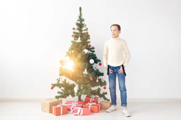 Vacaciones y concepto de la infancia de invierno - niño adolescente sonriente de pie cerca del árbol de Navidad sobre fondo blanco — Foto de Stock