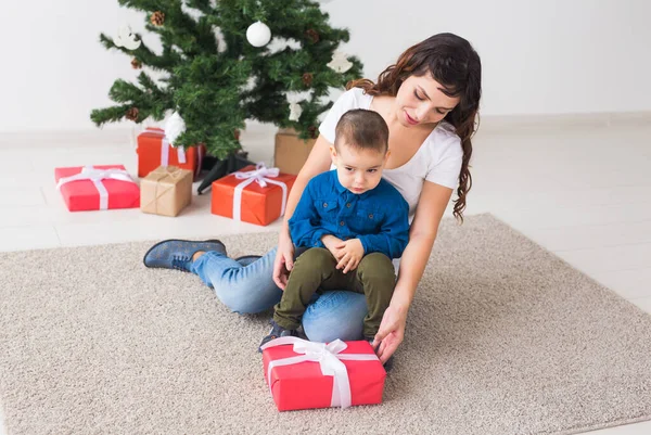 クリスマス、シングル親と休日のコンセプト-かわいい男の子開催クリスマスプレゼントのために彼の母親に家. — ストック写真