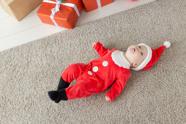 Прекрасная малышка празднует Рождество. Новый год. Младенец в рождественском костюме и шляпе санта, вид сверху

