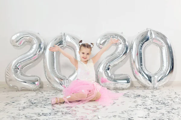 New year, holidays and celebration concept - Little girl sitting near with numbers balloons 2020