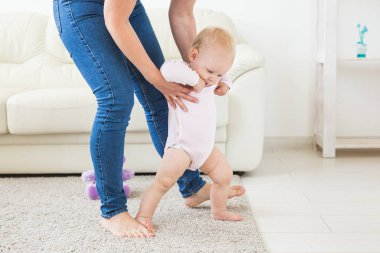 Beyaz güneşli oturma odasında yürümeyi öğrenen bebek bebek ilk adımları. Çocuk için ayakkabı.
